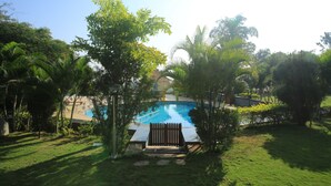 A swimming pool surrounded by lush greenery and a wooden deck. - Holiday Valley Nature Resorts (Denkanikota)