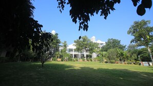 A large building with a prominent entrance and multiple windows, surrounded by a well-maintained lawn and various trees. - Holiday Valley Nature Resorts (Denkanikota)