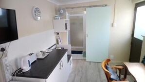 A compact kitchen with a black countertop, a microwave, a kettle, and a small refrigerator. There is a wooden chair and a table in the dining area. A sliding door leads to a balcony. - Welterusten Guesthouse (Cape Town)