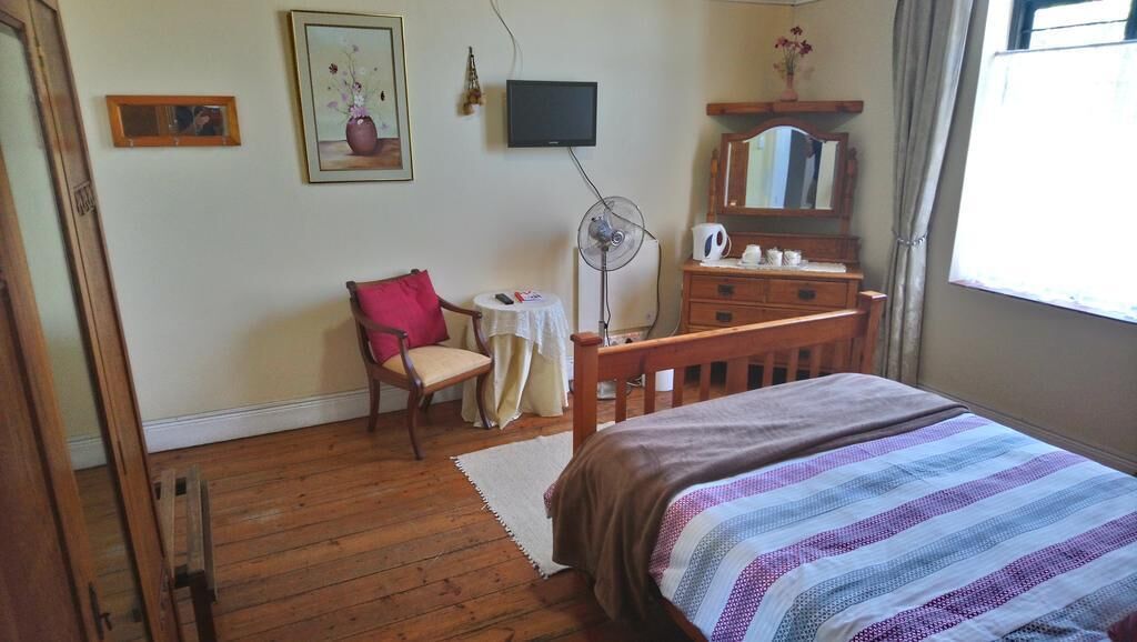 Un dormitorio con una cama de madera, una silla, una mesita, un televisor y un aparador.