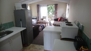 A compact kitchen with a refrigerator, microwave, and toaster. There is a dining area with a table and chairs, and a sofa with a view of the outdoors. - Welterusten Guesthouse (Cape Town)