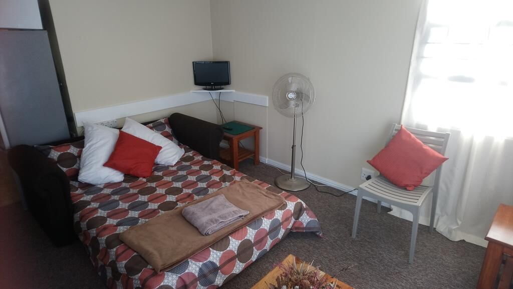 A hotel room with a bed, a TV, a standing fan, a small table, and a window with curtains.