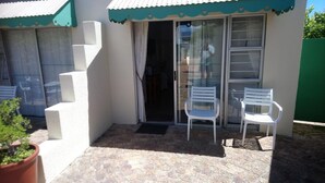 A small outdoor area with a sliding glass door, two white plastic chairs, and a potted plant. - Welterusten Guesthouse (Cape Town)