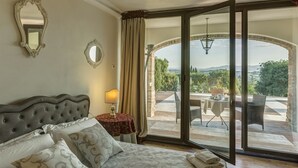 A bedroom with a large bed, a nightstand, a lamp, and a view of an outdoor patio with a table and chairs. - Torresassa, Montaione, Florence and Chianti (Montaione)