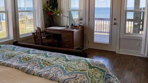 Une chambre dotée d’un grand lit, d’un bureau et offrant une vue sur l’océan grâce à de grandes portes-fenêtres coulissantes.
