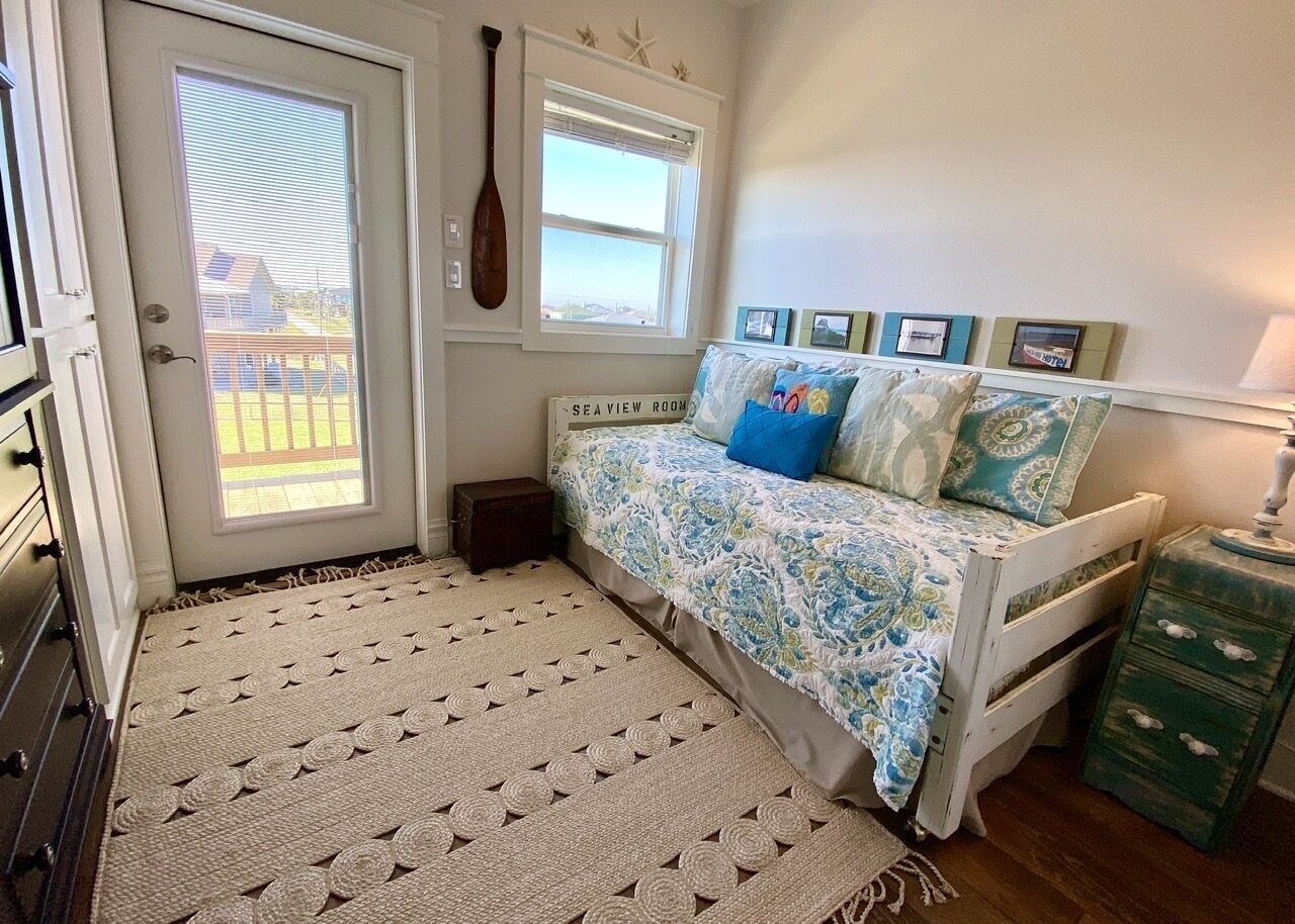 A bedroom with a bed, a small chest of drawers, a door with a view, and a wall-mounted starfish decoration.