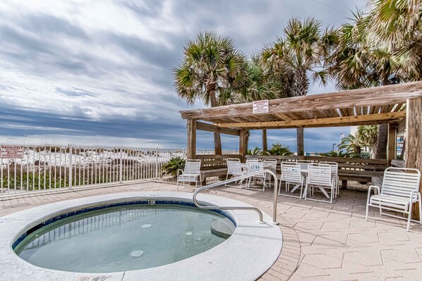 A pool area with a hot tub, lounge chairs, and a wooden pergola.