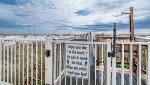 Une porte d’entrée menant à la plage, avec un panneau indiquant aux visiteurs de profiter de la journée, de faire attention à leur sécurité, de se protéger de la chaleur et de se laver les pieds avant de repartir.