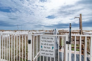 A beach entrance gate with a sign advising to enjoy the day, be safe, watch the heat, and wash feet when returning.
