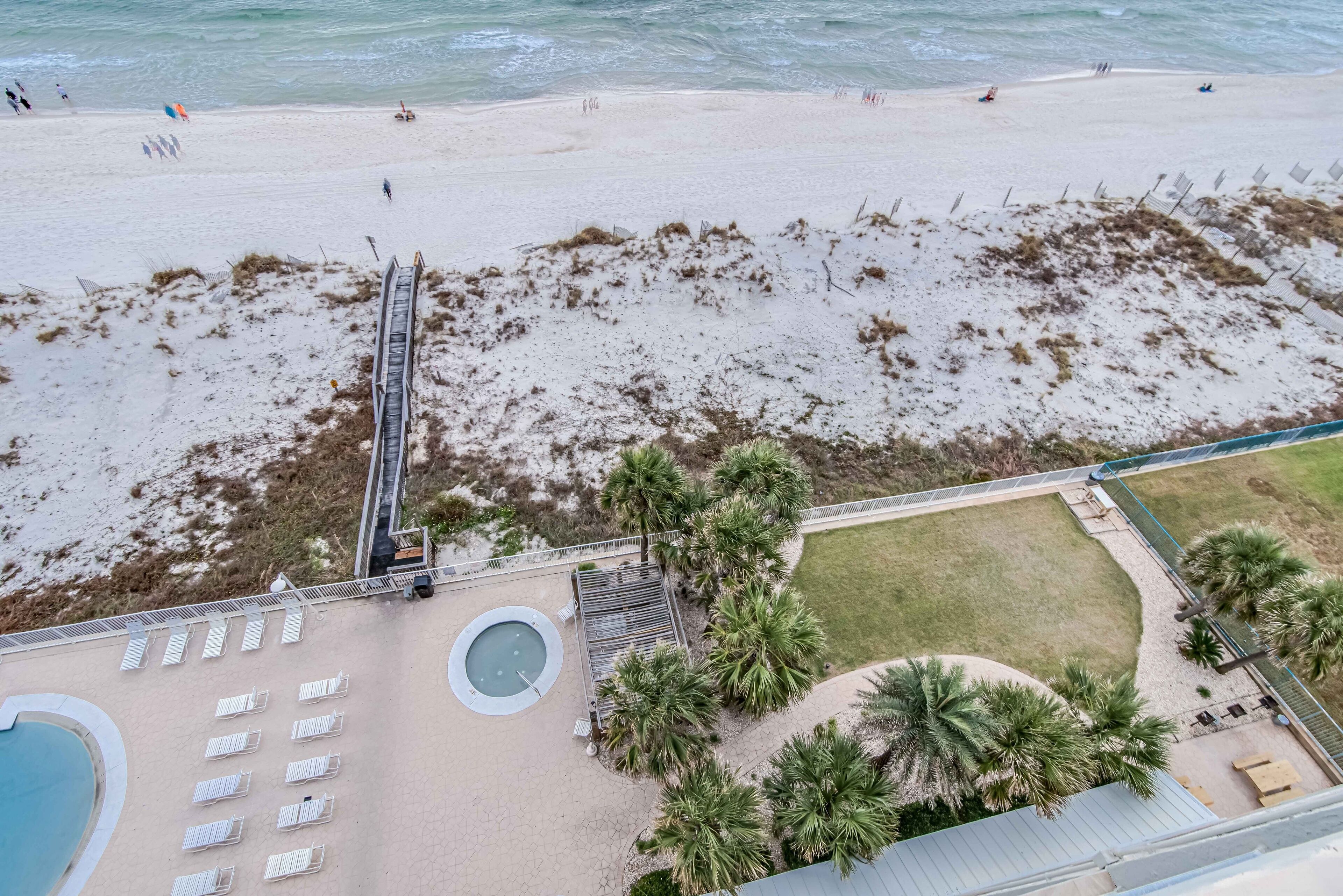 Vista aérea de una playa con zona de piscina, palmeras y una torre de salvavidas.