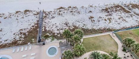 Vista aérea de una playa con zona de piscina, palmeras y una torre de salvavidas.