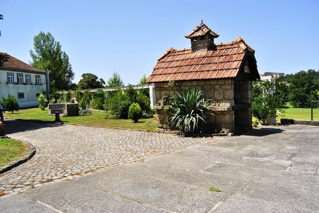 A stone building with a tiled roof, surrounded by a cobblestone path and greenery.