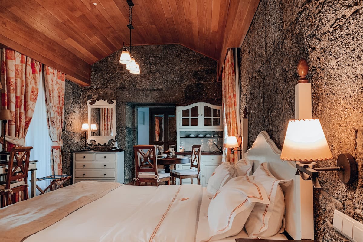 Ein gemütliches Schlafzimmer mit einem großen Bett, Holzboden, Steinwänden und einer rustikalen Küche im Hintergrund.
