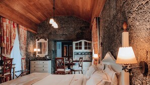 Un dormitorio acogedor con una cama grande, techo de madera, paredes de piedra y una cocina rústica al fondo.