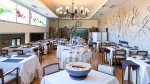 Un comedor amplio con varias mesas dispuestas para una comida, una lámpara de araña grande y un mural decorativo en la pared.