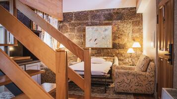Um quarto acolhedor com uma escada de madeira, uma cama, uma poltrona estampada e uma parede de pedra.