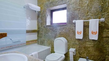Un baño con pared de piedra, una bañera, un inodoro y un lavabo.