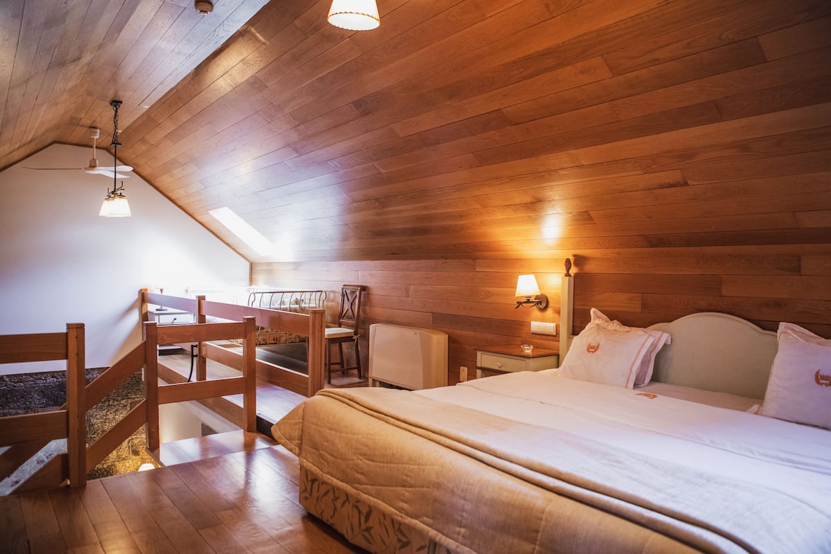 Ein gemütliches Zimmer mit Holzbalkendecke, einem Bett mit weißer Bettwäsche, einem Schreibtisch und einem Stuhl.