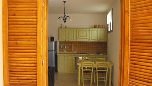 Eine kompakte Küche mit Holzausbau, einem Esstisch mit Stühlen, einem Kühlschrank und einer Pendelleuchte.