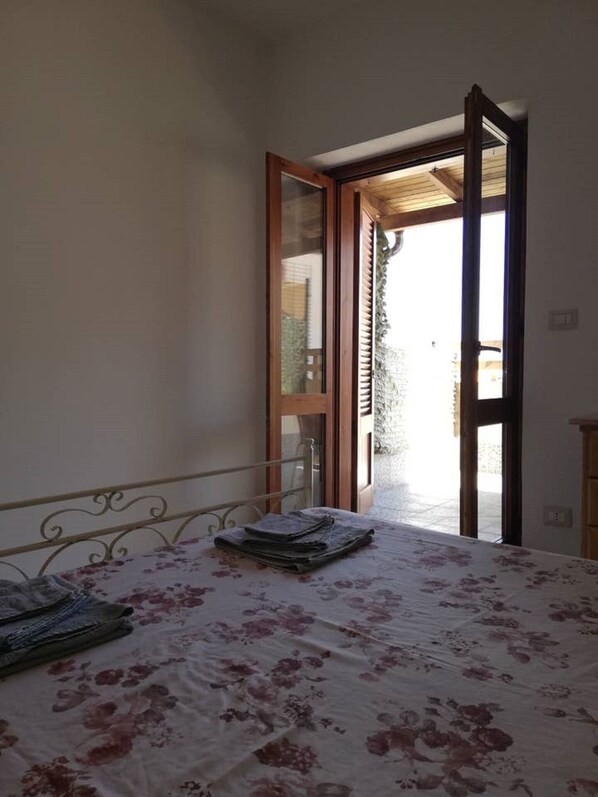 A bedroom with a bed, a window, and an open door leading to a balcony.