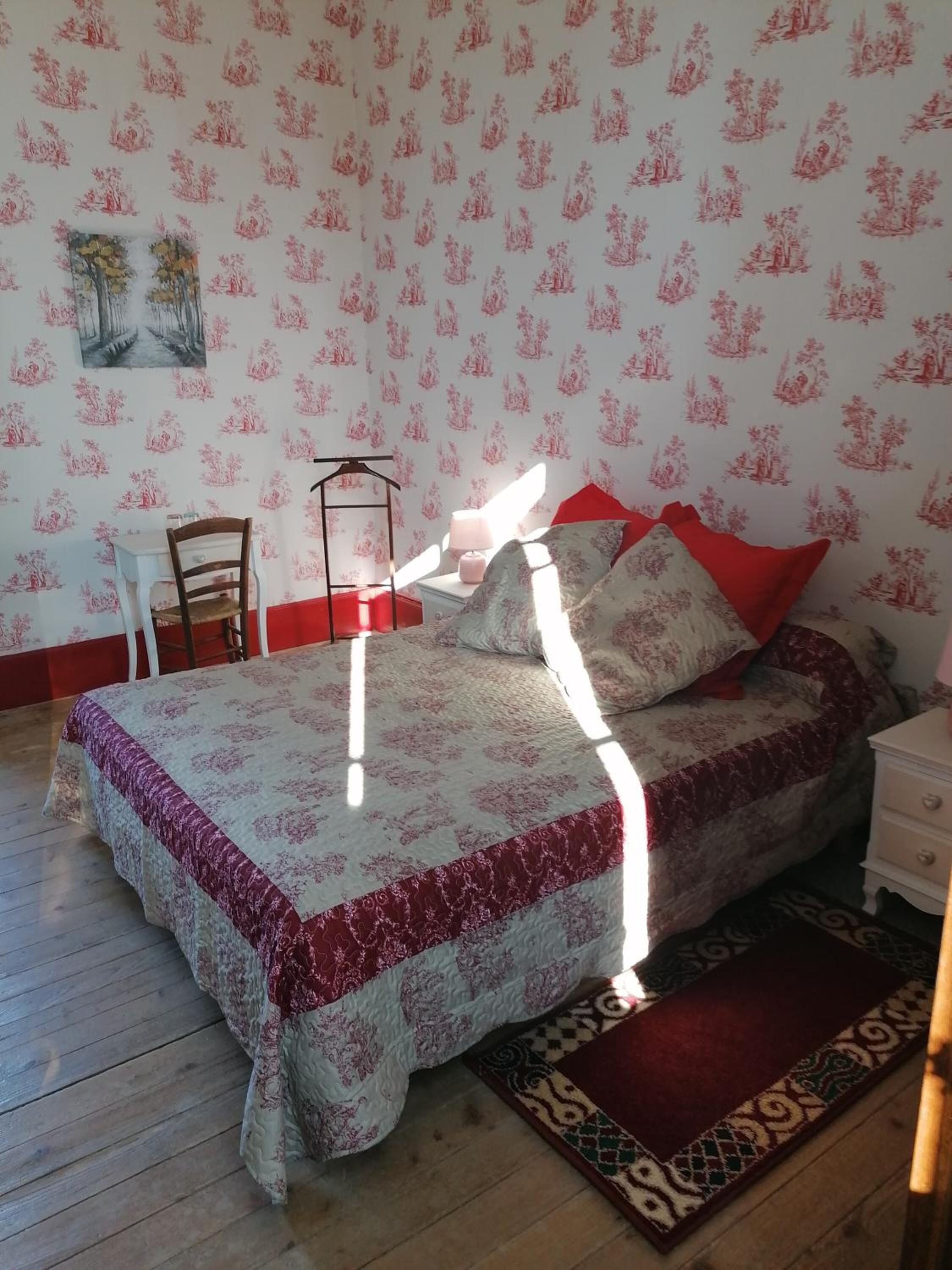 Un dormitorio con cama, una silla, una mesita de noche y un papel tapiz estampado.