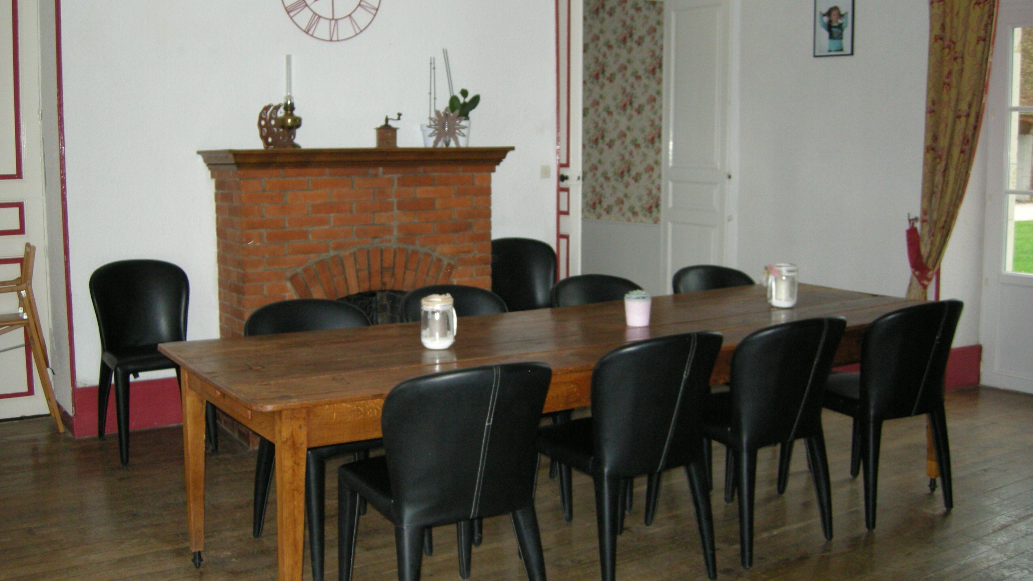 Ein Esszimmer mit Holztisch und schwarzen Stühlen, einem Kamin aus Ziegelsteinen und einer Uhr an der Wand.