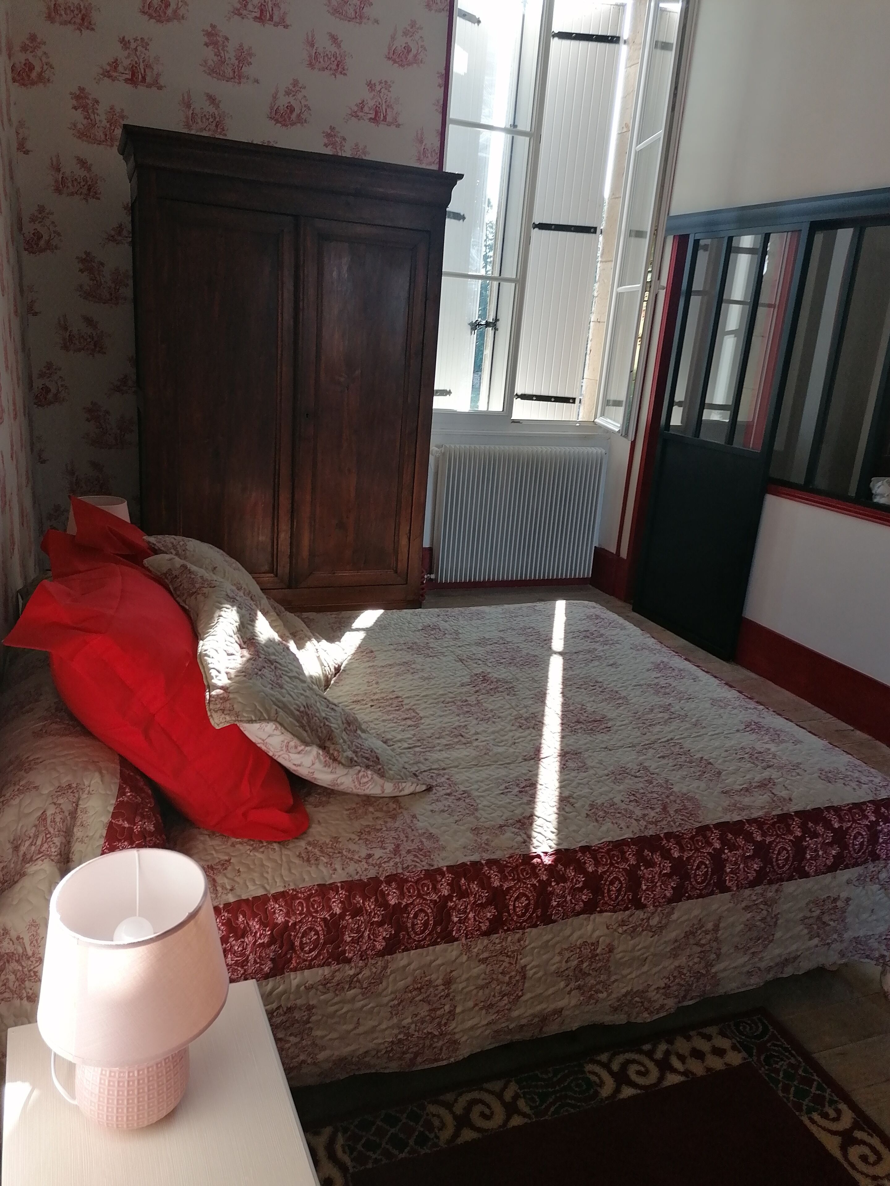 A bedroom with a bed, a wooden wardrobe, a radiator, and a window.