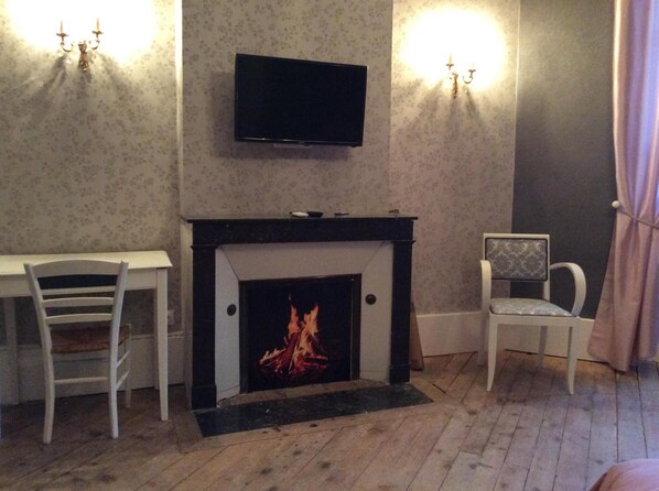 Una habitación con chimenea, televisor montado en la pared, escritorio y una silla.