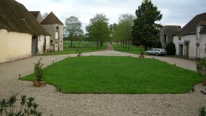 A courtyard with a gravel path leading to a green lawn, surrounded by buildings with traditional architecture.