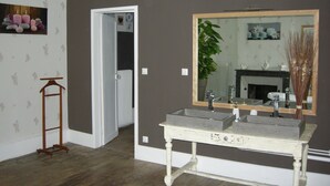 A bathroom with a double sink, a large mirror, a wooden floor, and a door leading to another room.
