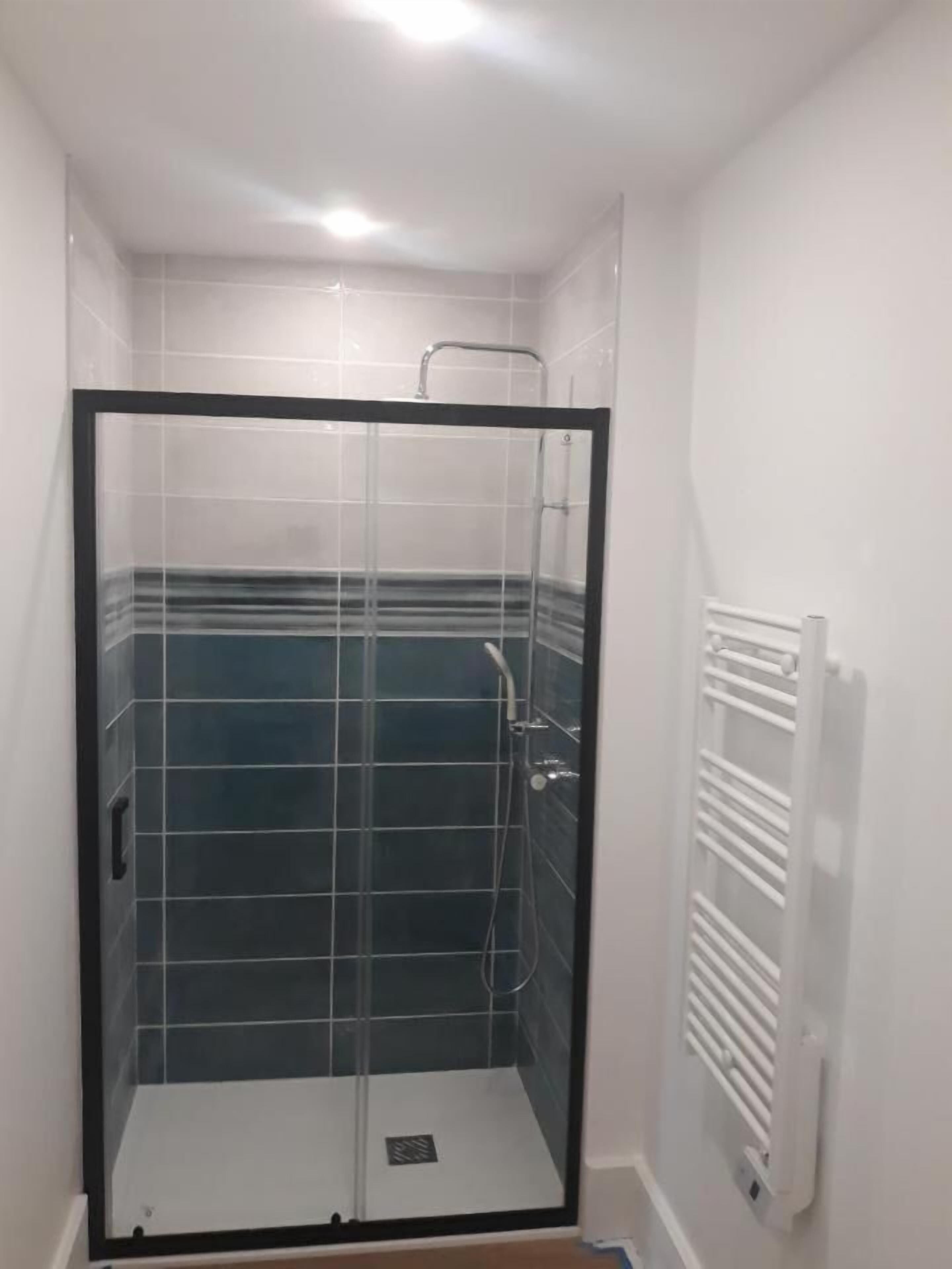 A small, enclosed shower area with a glass door, tiled walls, and a white radiator.