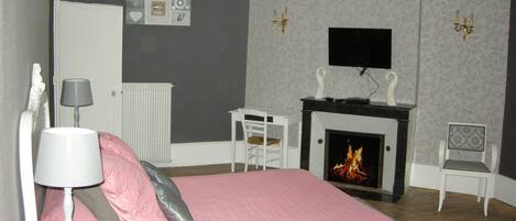 Une chambre à coucher comprenant un lit, une table de chevet avec une lampe, une chaise, une cheminée et un téléviseur fixé au mur.