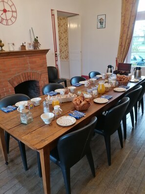 A dining room with a brick fireplace, a long wooden table set for breakfast, and black chairs. - Chateau de Chavannes (Tresnay)
