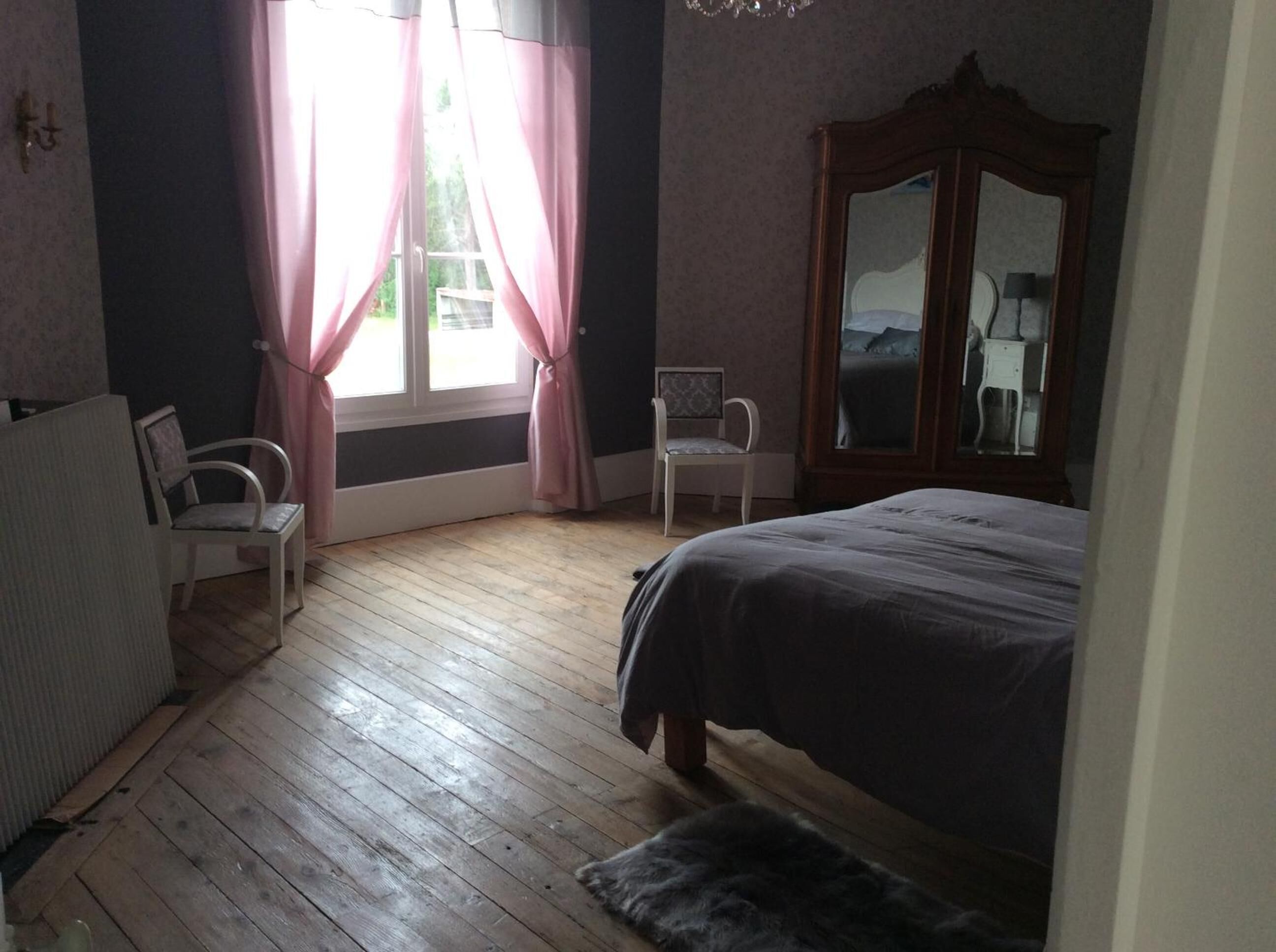 A bedroom with a wooden floor, a bed, a chair, and a wardrobe.