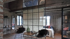 A rustic room with a wooden floor, a large window with a view, a bed with a white bedspread, and a table with chairs. - Siggesta Gård (Värmdö)