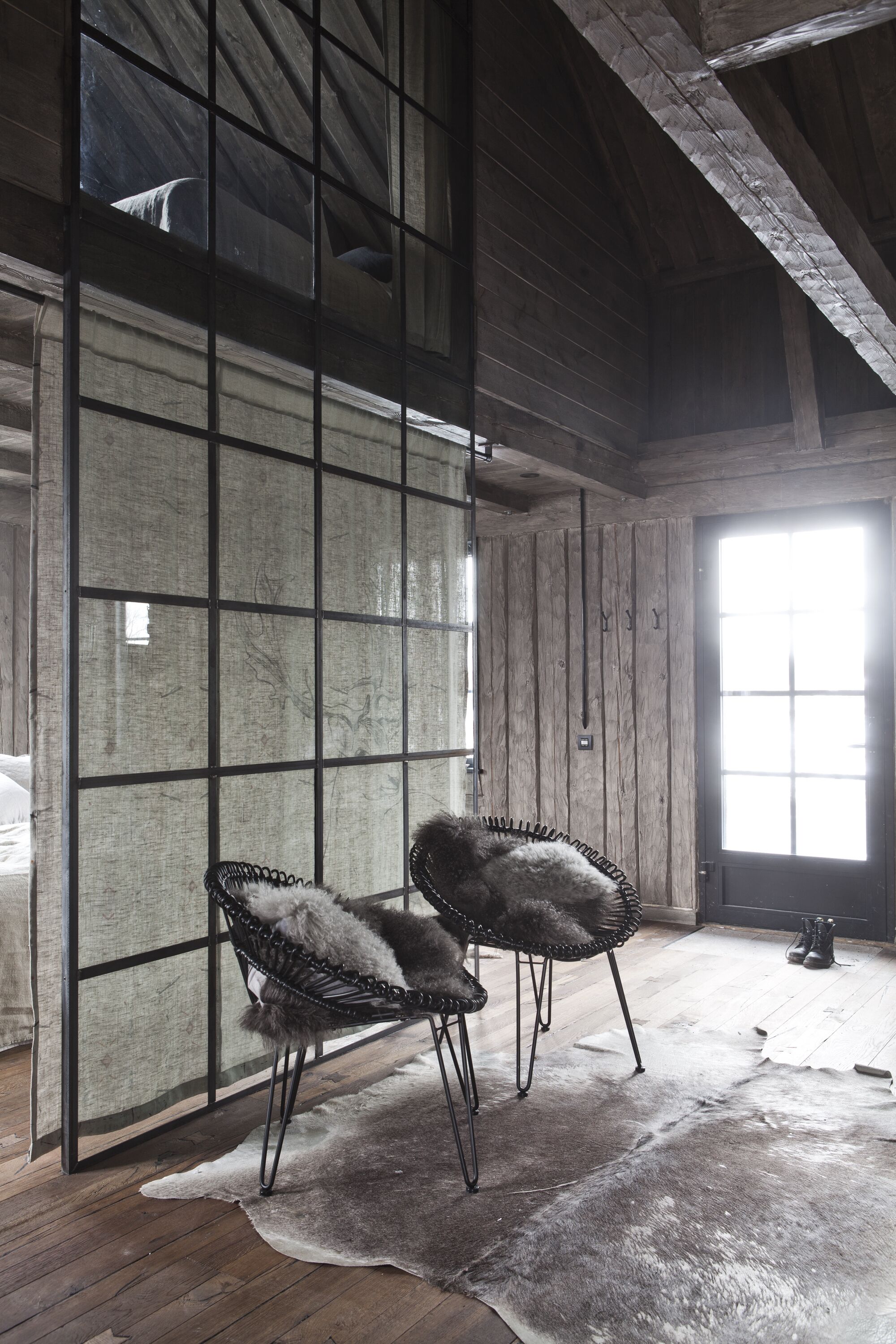 Una habitación con paredes de madera, un ventanal grande, dos sillas y un manto de piel.
