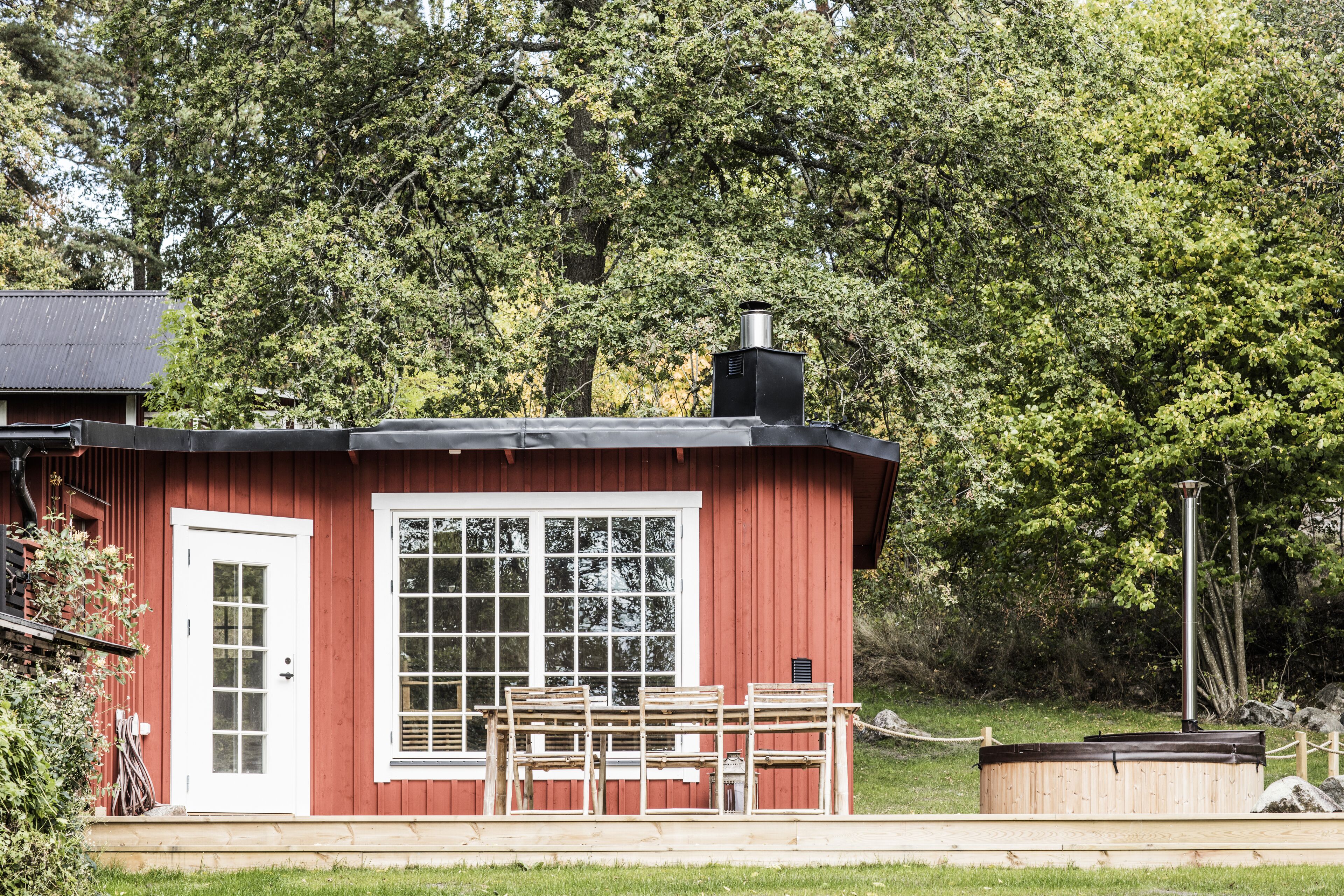 A red wooden cabin with a large window, a door, and a chimney.