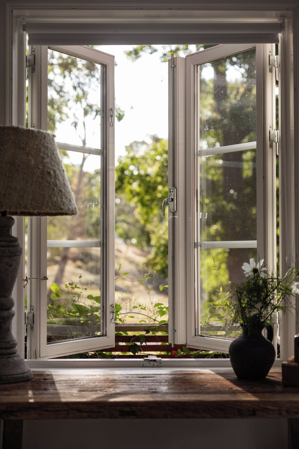A room with a large window, a lamp, and a vase with flowers.