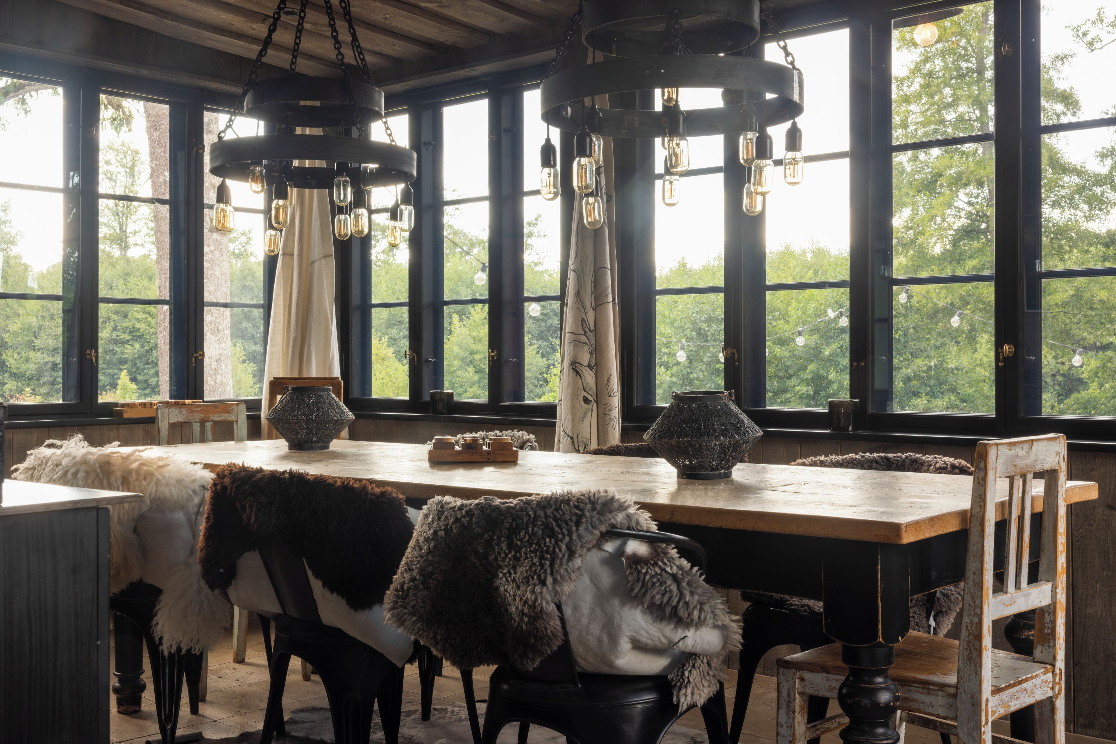 A rustic dining area with a long wooden table, chairs, and hanging light fixtures.