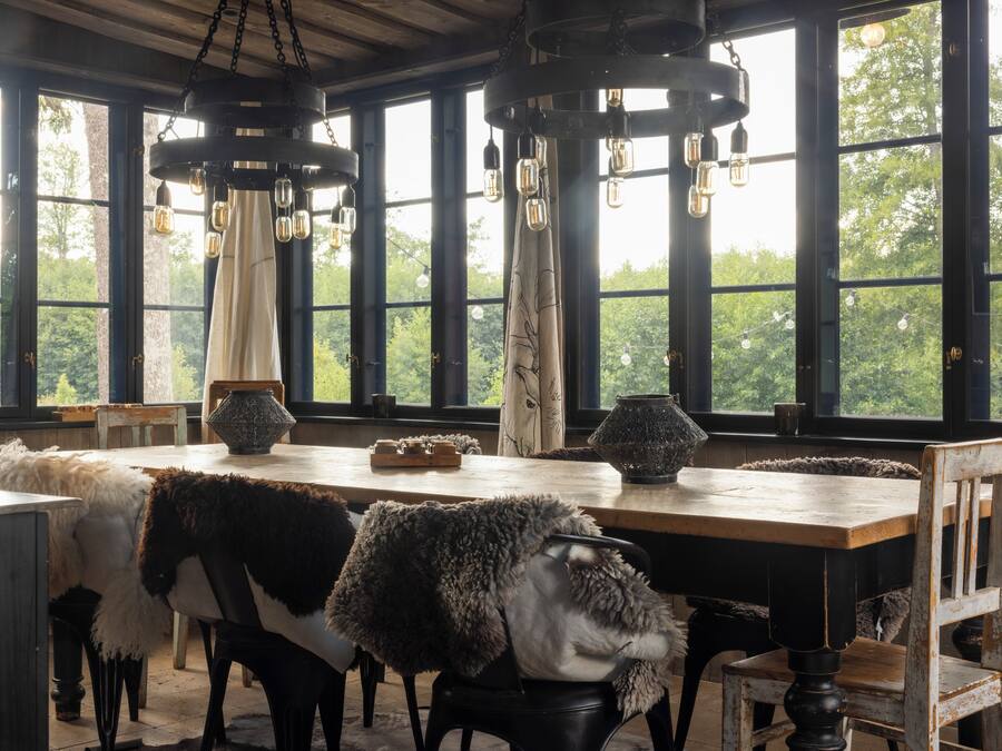 A rustic dining area with a long wooden table, chairs, and hanging light fixtures.