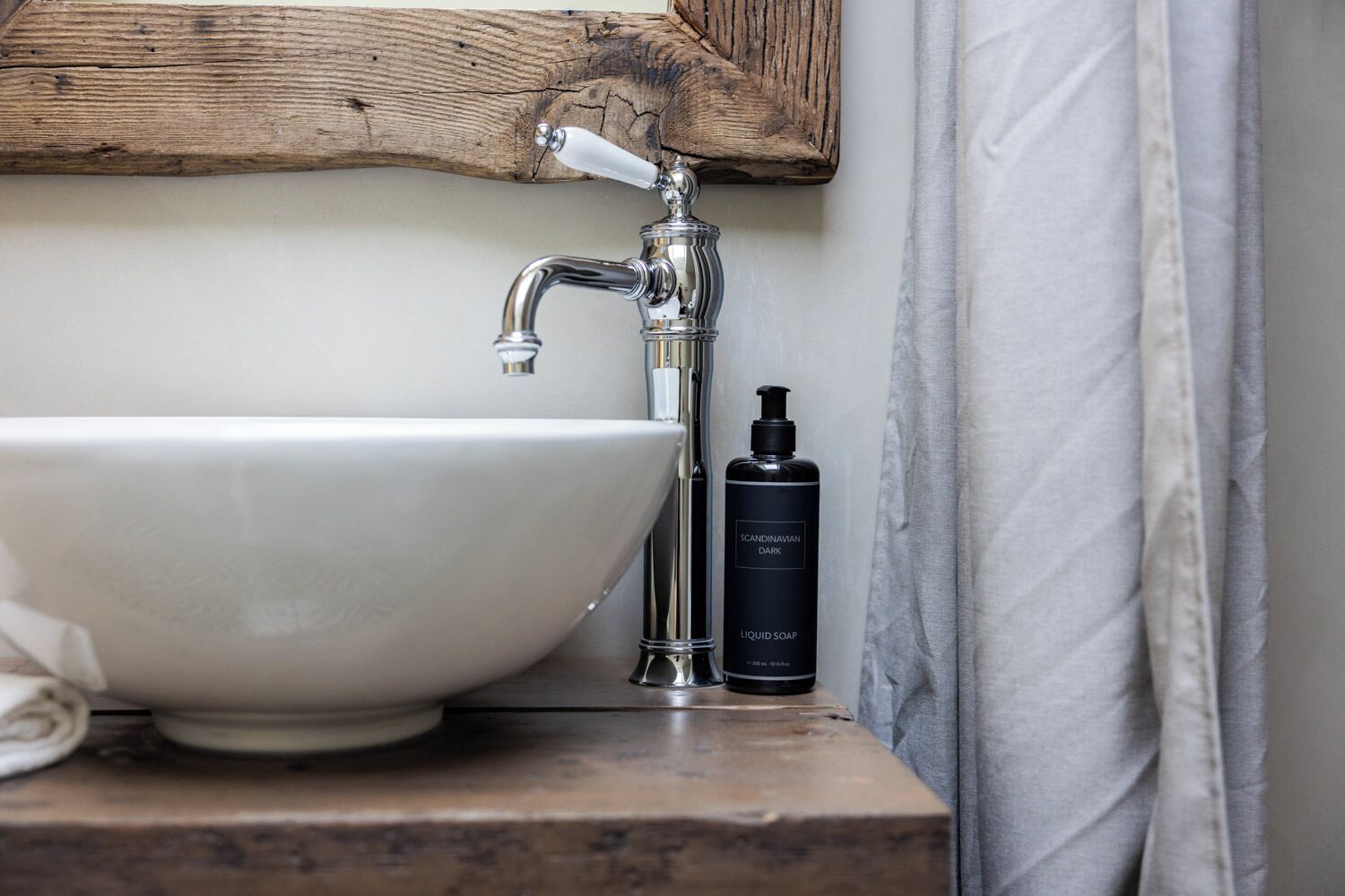 A bathroom with a white sink, a wooden shelf, and a bottle of liquid soap.