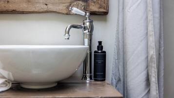 A bathroom with a white sink, a wooden shelf, and a bottle of liquid soap.