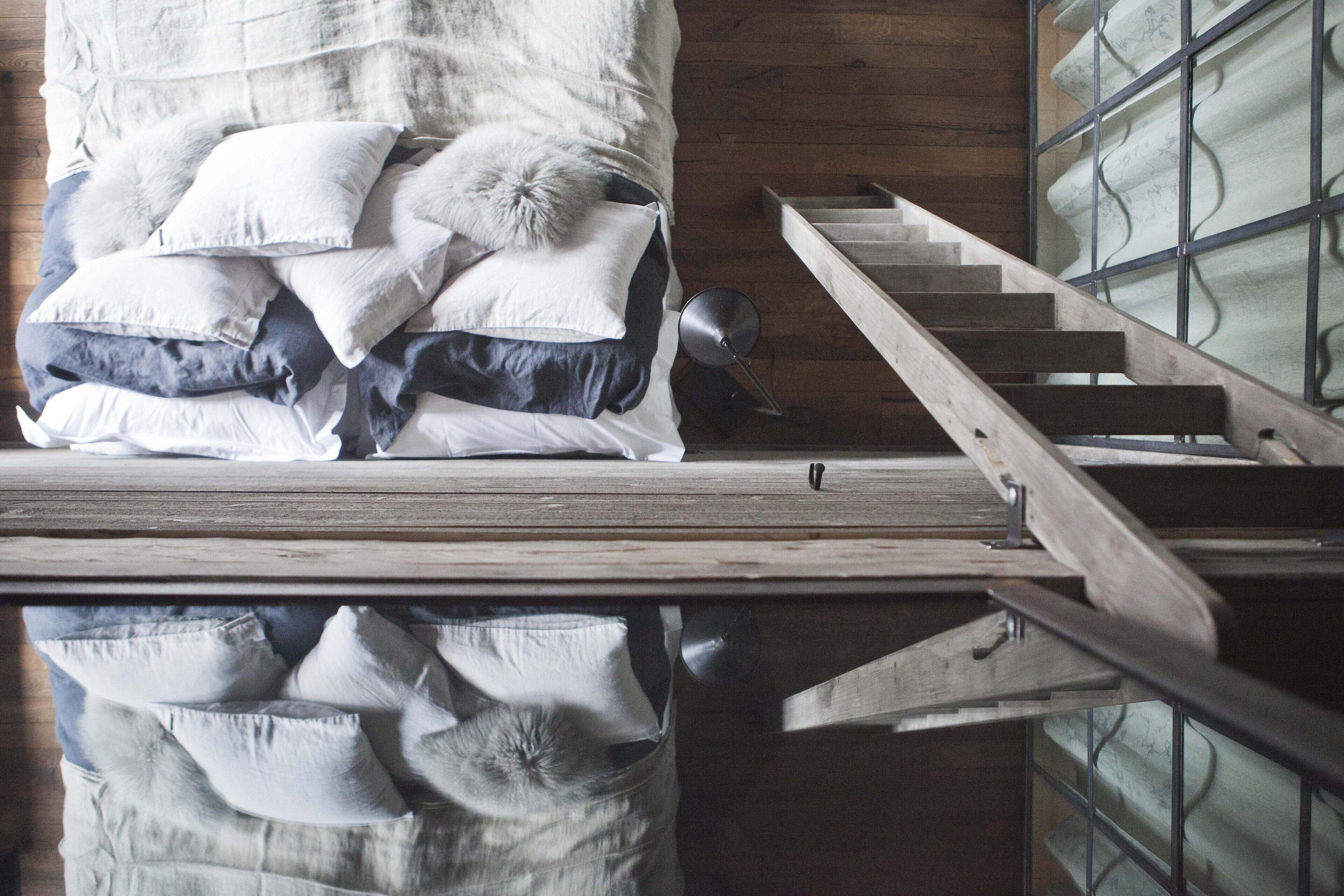 A bedroom with a wooden floor, a bed with multiple pillows, and a wooden staircase.