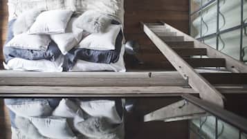 Un dormitorio con suelo de madera, una cama con muchas almohadas y una escalera de madera.