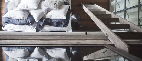 A bedroom with a wooden floor, a bed with multiple pillows, and a wooden staircase.