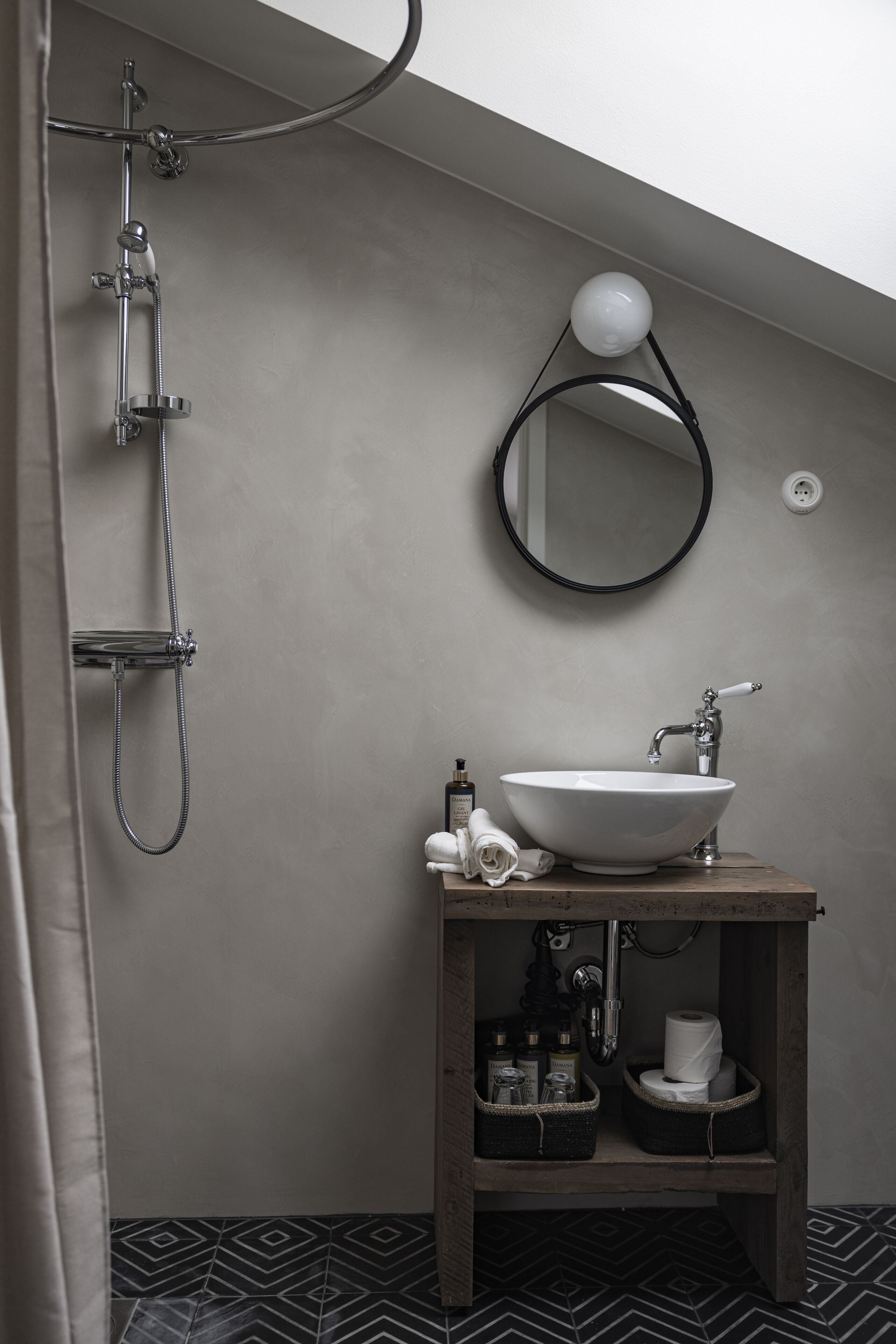 Een moderne badkamer met een vrijstaand bad, een ronde spiegel en een houten wastafelmeubel met wastafel en opbergruimte.