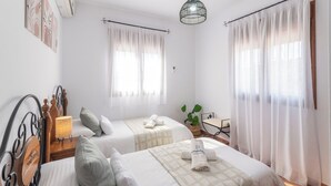 Une chambre d’hôtel avec deux lits, une table de chevet avec une lampe, une petite table avec une plante et une chaise.