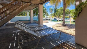 Een overdekt buitengebied met lounge stoelen, een zwembad, palmbomen en uitzicht op het water.