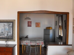 A compact kitchen with a dining table, chairs, a refrigerator, and a wooden cabinet.