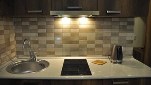 A kitchen with a stainless steel sink, a black stovetop, and a kettle on the counter. - New Gudauri Block 4 - Ski4Life (Kazbegi)